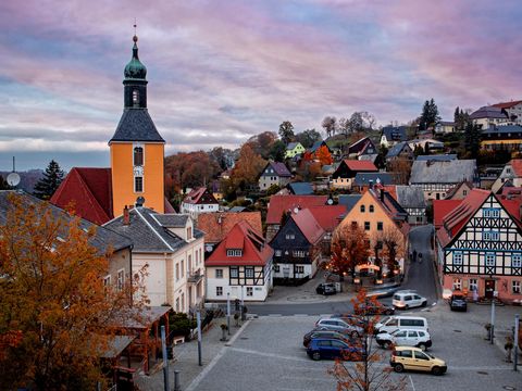 Blick von Burg Hohnstein auf kleine Kirche und Fachwerkhäuser, blaue und lila Wolken am Himmel.