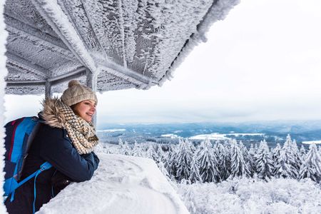 Frau mit Mütze und Schal lehnt an einem frostigen Geländer und blickt auf eine winterliche Landschaft.