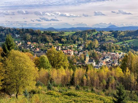 Blick auf Sebnitz: Häuser und Kirchturm umgeben von bewaldeten Hügeln unter blauem Himmel.