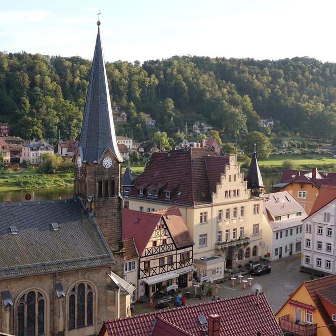 Blick auf eine malerische Stadt mit historischen Gebäuden und einem Kirchturm, umgeben von grünen Hügeln.