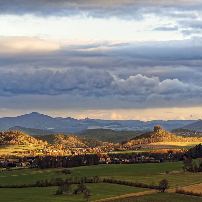 Landschaft mit sanften Hügeln, bewölktem Himmel und Sonnenstrahlen, die auf Felder scheinen.