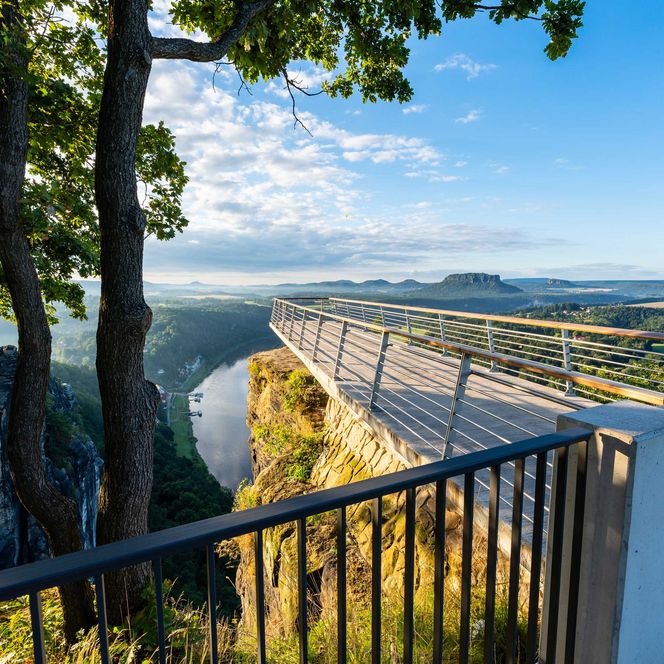 Aussichtsplattform an der Bastei mit Geländer, Blick auf eine Landschaft mit Bergen und Fluss im Hintergrund.
