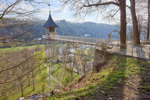 Alter Personenaufzug in Bad Schandau, grauer Turm, üppige grüne Umgebung.