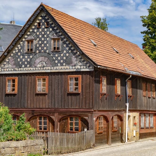 Fachwerkhaus mit rotem Satteldach, Holzverkleidung und grüner Umgebung.