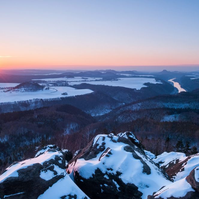 Sonnenaufgang über schneebedeckten Felsen und Tälern, mit sanften Farben am Himmel.