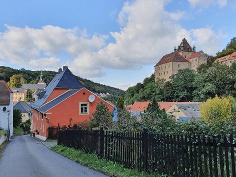 Mittelalterliche Burg Kuckuckstein auf Hügel, umgeben von grünen Bäumen und blauem Himmel, im Vordergrund Häuser der Stadt Liebstadt..
