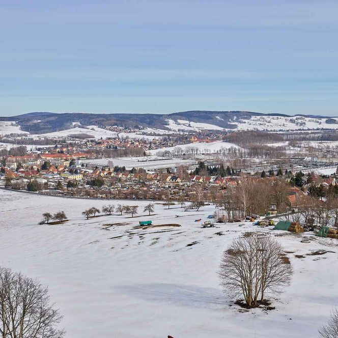 Schneebedeckte Landschaft mit Bergen im Hintergrund und einem klaren blauen Himmel.