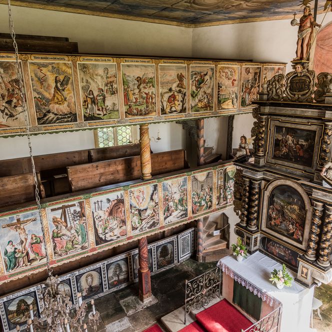 Blick auf eine historische Kirche mit kunstvollen Wandmalereien und einem altarähnlichen Aufbau.
