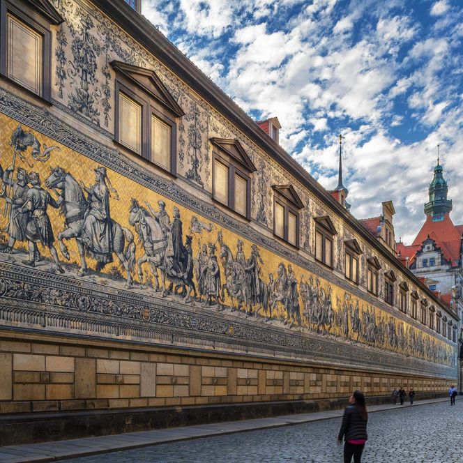 Historisches Gebäude mit goldenen Reliefs an der Wand und bewölktem Himmel.