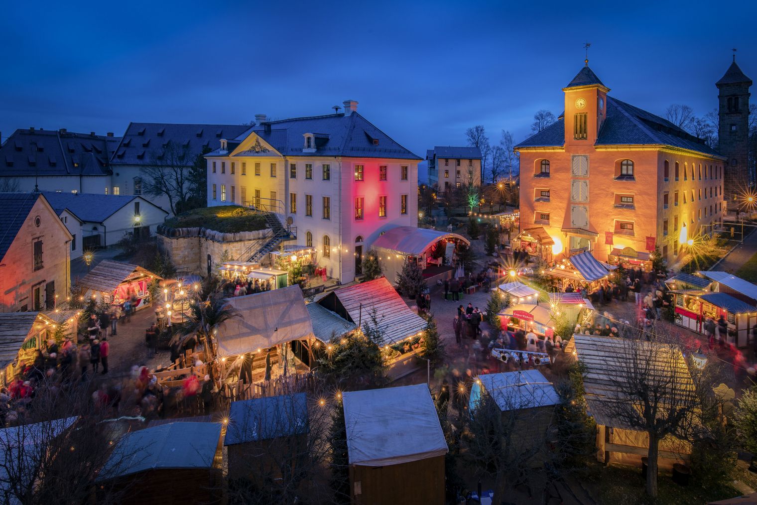 Historisch-Romantischer Weihnachtsmarkt Festung Königstein am Abend mit festlich beleuchteten Ständen und Gebäuden bei Dämmerung.