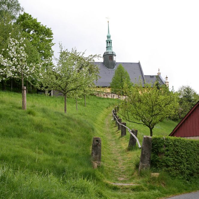 Grüne Wiese mit Obstbäumen, im Hintergrund ein Gebäude mit einer Kupferkuppel und einem roten Schuppen.