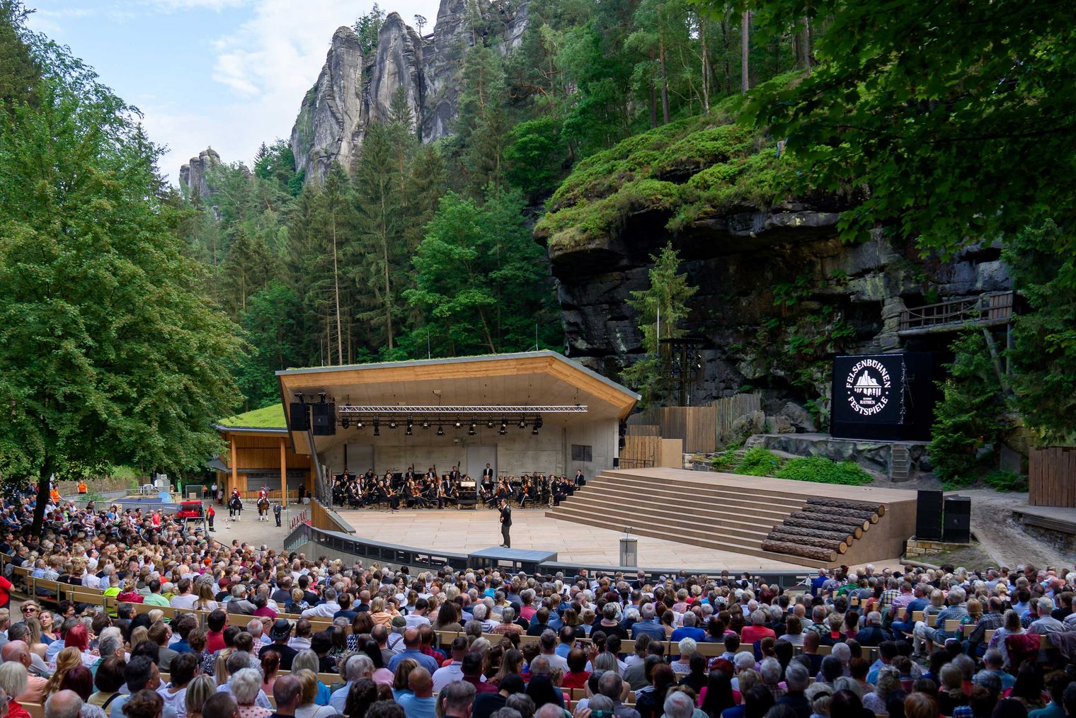 Freiluftbühne Felsenbühne Rathen mit Publikum im Nationalpark Sächsische Schweiz, umgeben von Felsen und Bäumen.