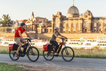 Zwei Radfahrer fahren vor historischem Gebäuden der Stadt Dresden entlang des Flusses Elbe