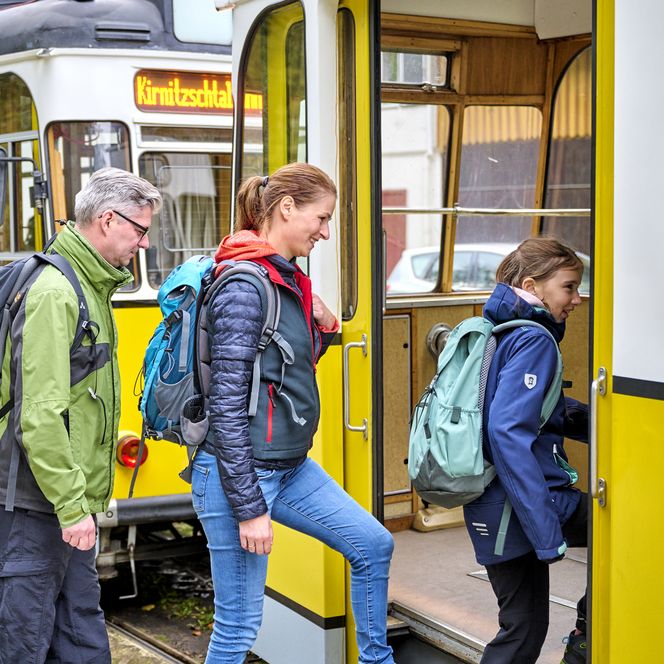 Drei Personen mit Rucksäcken steigen in eine Straßenbahn ein.