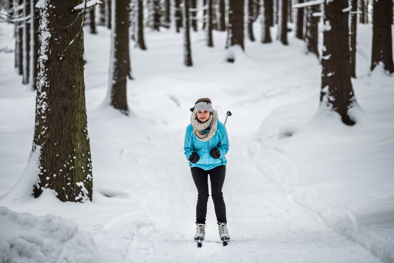 Frau in blauer Jacke und schwarzer Hose beim Skilanglauf in verschneitem Wald.