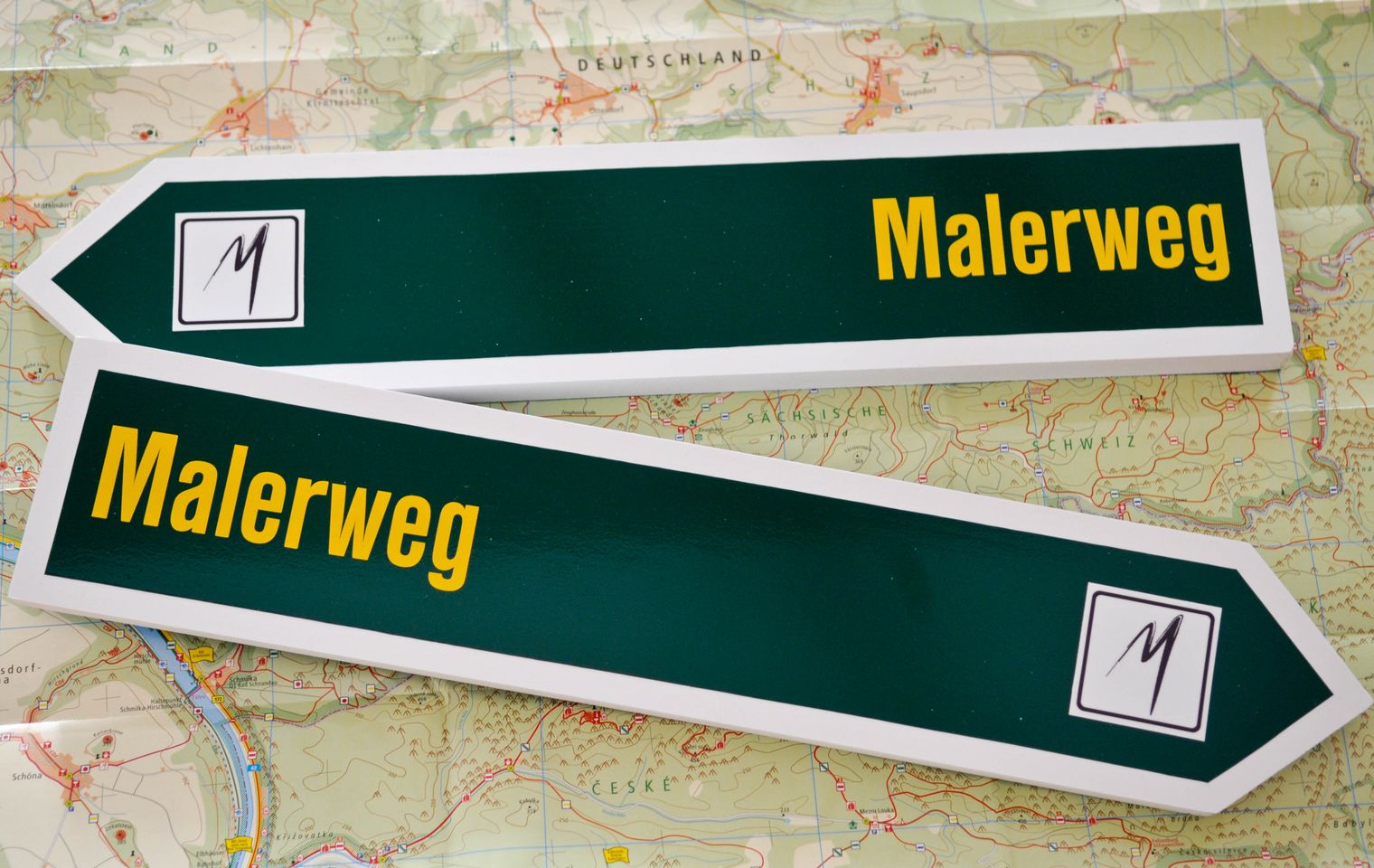 Zwei Schilder als Malerweg-Wegweiser in grüner Farbe mit Logo.