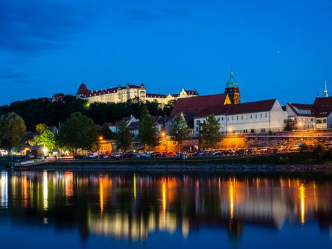 Blick auf Pirna am Abend mit Elbe, Schloss Sonnenstein und historischen Häusern im Hintergrund. Dunkler klarer Himmel.