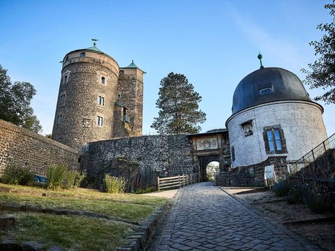 Burg Stolpen mit Türmen, grüner Hügel im Vordergrund, blauer Himmel im Hintergrund.