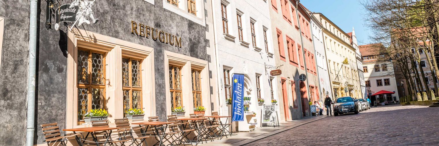 Bunte Häuserfassaden in der Pirnaer Altstadt entlang einer gepflasterten Straße bei sonnigem Wetter.