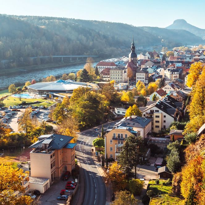 Blick auf eine malerische Stadt im Herbst mit bunten Laubbäumen und einem Fluss im Hintergrund.