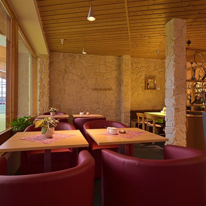 Gemütliches Restaurant mit roten Sesseln, Holztischen und großen Fenstern.