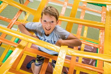Junge klettert fröhlich durch eine gelbe Spielgerüststruktur im Kindertobeland des Solivital Sebnitz