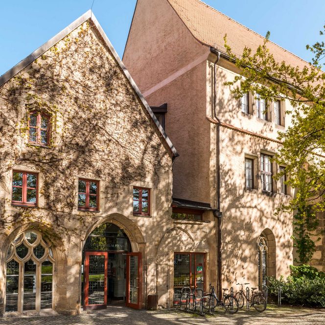 Historische Gebäude mit Steinfassade und bunten Fenstern, umgeben von Bäumen.