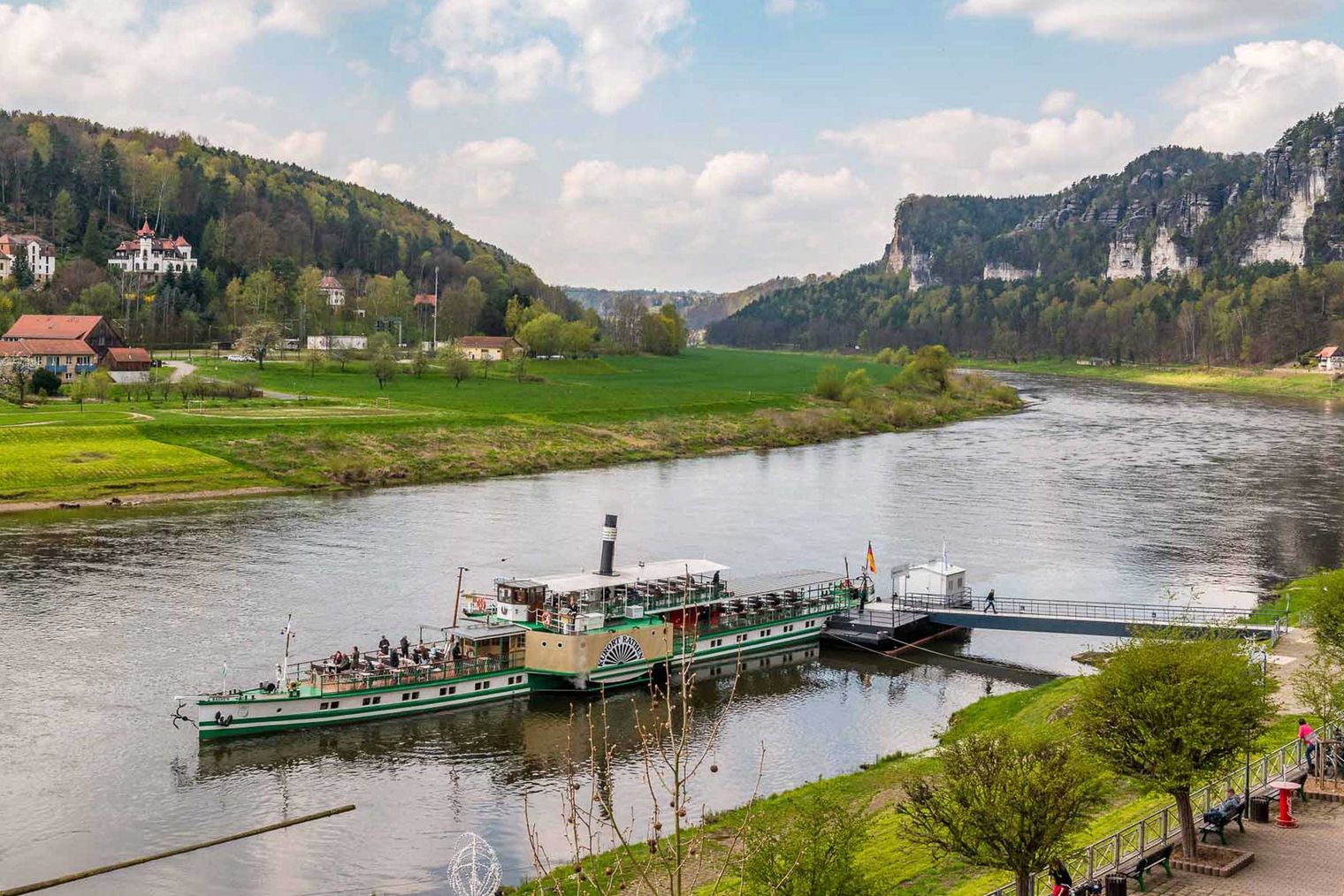 Flusslandschaft mit Dampfer und bewaldeten Hügeln im Hintergrund.