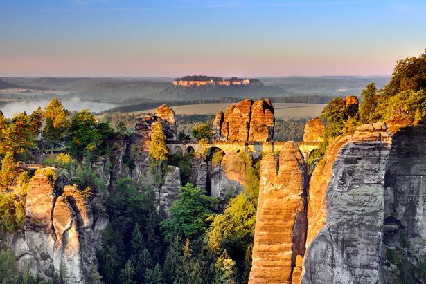 Felsformation mit Basteibrücke und Bäumen in der Sächsischen Schweiz, bewölkter Himmel.