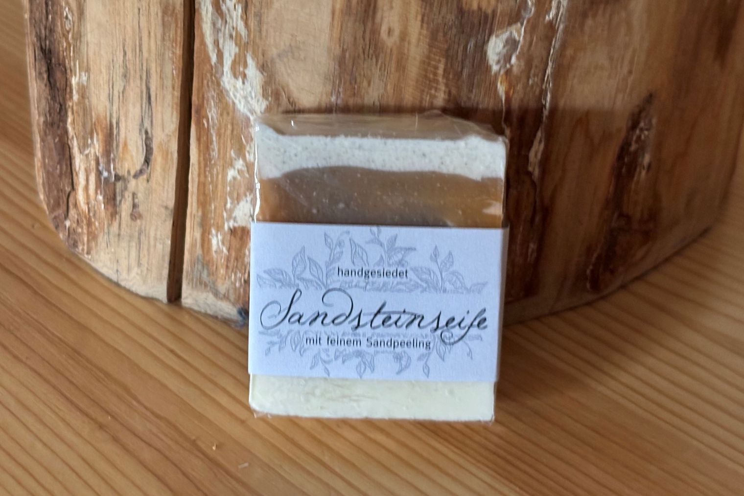 Sandsteinseife Auf einem Holztisch steht eine quadratische Seife mit der Aufschrift "Sandsteinseife".