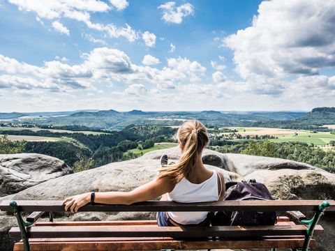 Eine Frau sitzt auf einer Bank mit Ausblick auf die Landschaft der Sächsischen Schweiz.