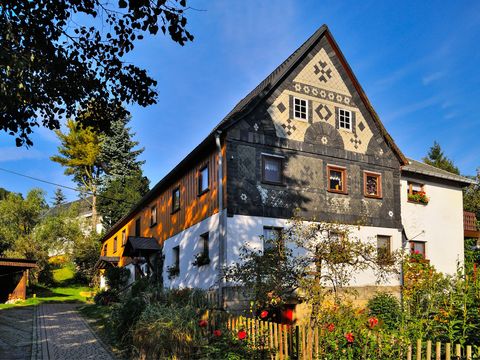 Umgebindehaus in Hinterhermsdorf mit Holzstruktur, blühender Garten, blauer Himmel.