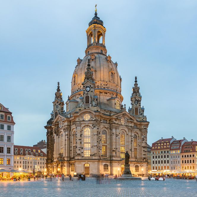 Frauenkirche in Dresden, beleuchtet bei Dämmerung, umgeben von historischen Gebäuden und Weihnachtsständen.