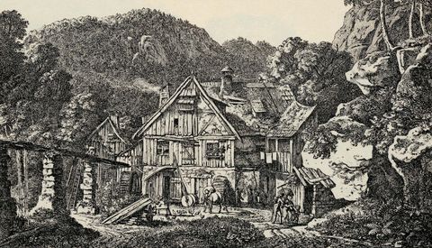 Historische Mühle in einer ländlichen Umgebung, umgeben von Bäumen und Hügeln.