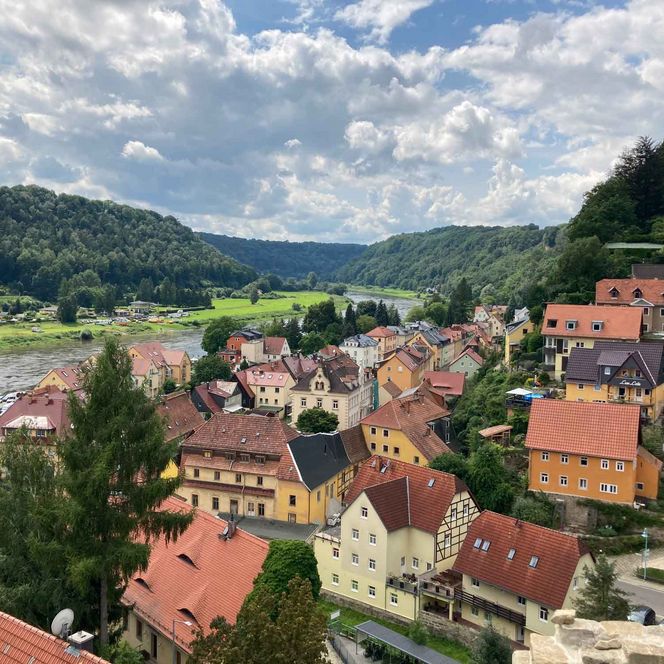 Blick auf ein malerisches Dorf mit bunten Häusern, umgeben von grünen Hügeln und bewölktem Himmel.