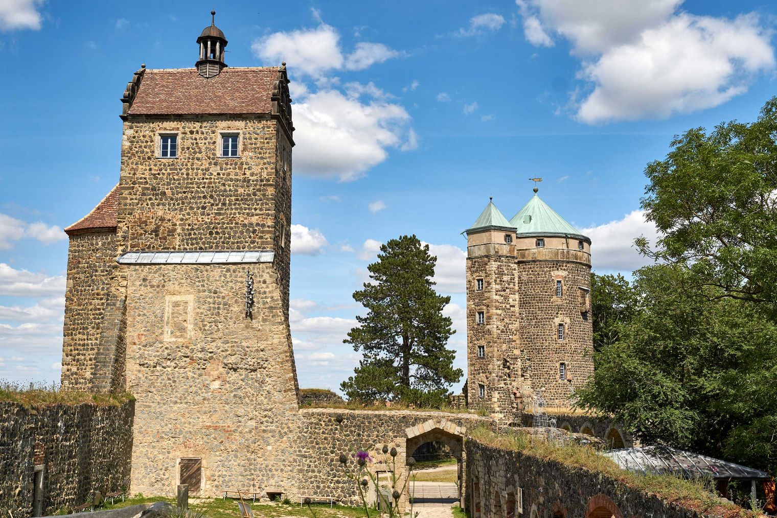 Drei historische Türme der Burg Stolpen mit unterschiedlichen Dächern unter einem blauen Himmel mit Wolken.