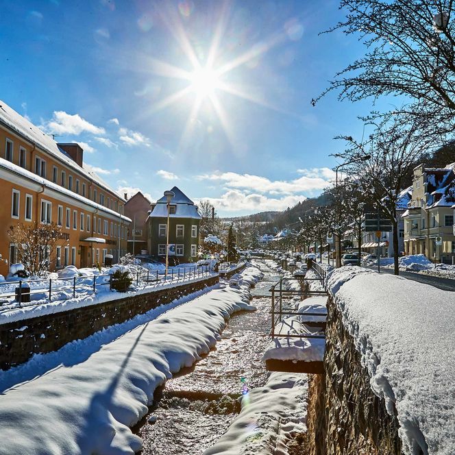 Winterlandschaft mit schneebedeckten Gebäuden, einem Kanal und strahlendem Sonnenschein.