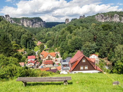 Felsenlandschaft mit grünen Bäumen, Kurort Rathen und Felsen im Hintergrund.