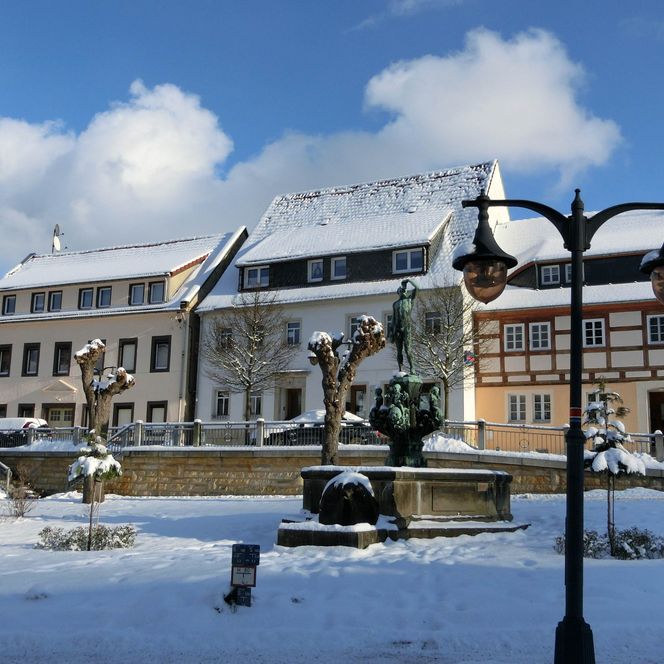 Schneebedeckte Stadtansicht mit historischen Gebäuden und einer Statue im Vordergrund.