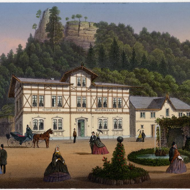 Historisches Gebäude mit Fachwerk, umgeben von Bäumen und einem Hügel im Hintergrund. Menschen und Pferde sind sichtbar.