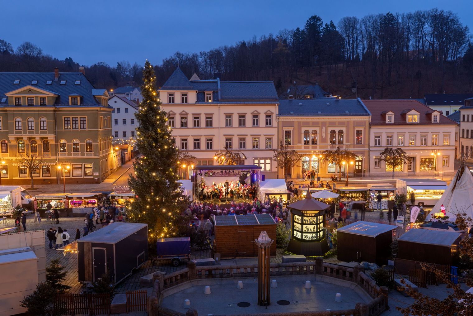 Weihnachtsmarkt mit festlich beleuchteten Ständen und einem großen Weihnachtsbaum in der Mitte.