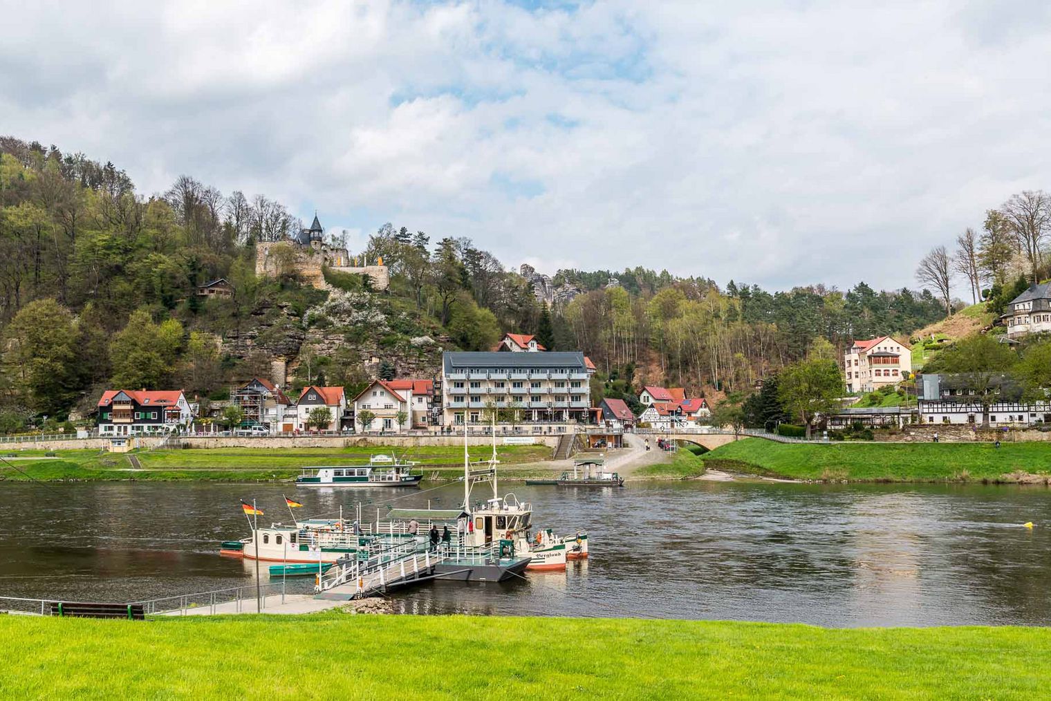 Blick auf ein malerisches Ufer mit Booten, umgeben von grünen Hügeln und einem Hotel im Hintergrund.