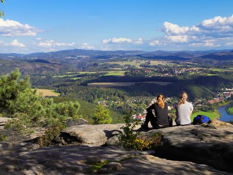 Blick vom Lilienstein auf die Elbe, im Vordergrund zwei Personen die auf Bad Schandau im Sommerlicht blicken.
