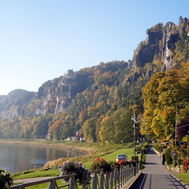 Blick auf einen Fluss, umgeben von bunten Bäumen und steilen Felsen im Hintergrund.