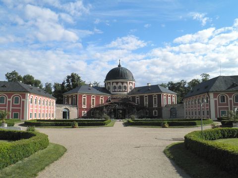 Schloss auf einem Hügel bei Sonnenuntergang, umgeben von Bäumen und Weinbergen.