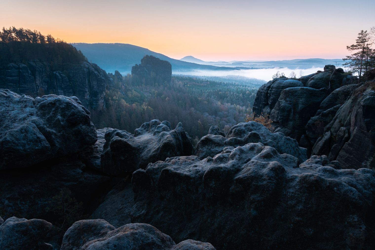 Sonnenaufgang über einer felsigen Landschaft mit Bäumen und Wolken am Himmel.