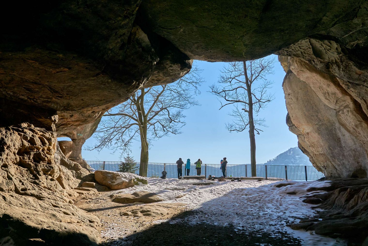 Blick auf das Felsentor Kuhstall auf Bäume und eine Gruppe von Menschen im Freien.