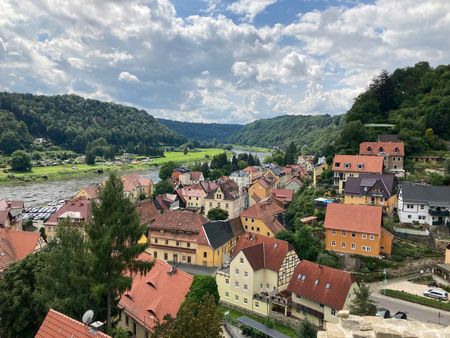 Blick auf ein malerisches Dorf mit bunten Häusern, umgeben von grünen Hügeln und bewölktem Himmel.