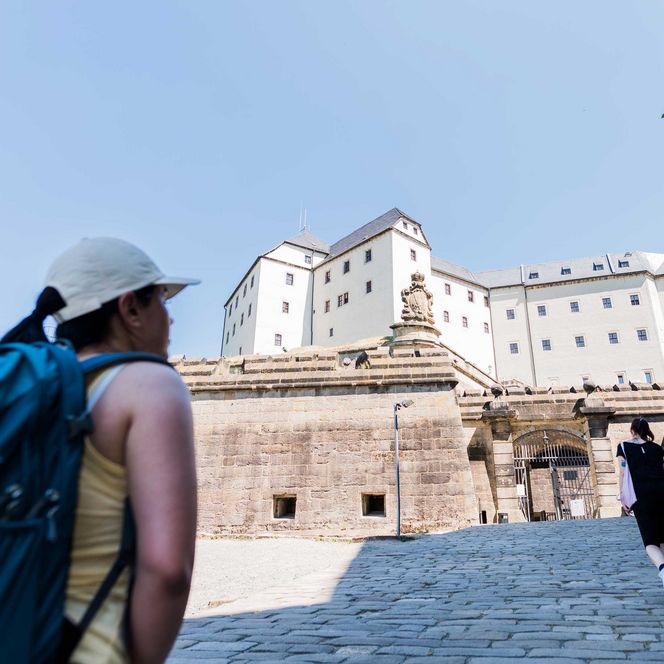 Wanderer mit Rucksack schaut auf die große, historische Festung Königstein.