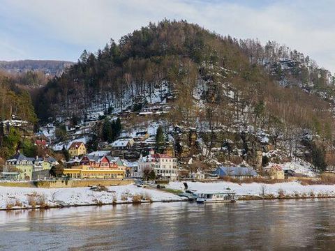Blick auf ein Dorf mit Fachwerkhäusern im Winter, umgeben von bewaldeten Hügeln und bewölktem Himmel.
